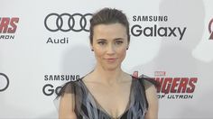 a woman in a black dress posing for the camera on a red carpet with an avengers logo behind her