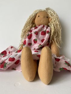 a stuffed doll with blonde hair sitting on a white surface wearing a pink and red dress