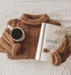 there is a book and sweater on the bed next to a cup of hot chocolate