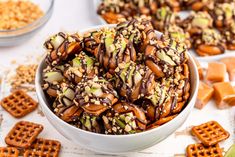 a bowl filled with chocolate covered pretzels next to crackers and other snacks