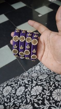 a person holding some kind of purple and gold bracelet in their hand on a black and white tile floor