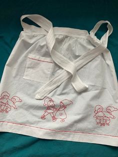 a white bag with red embroidered designs on it sitting on a green surface next to a pair of scissors