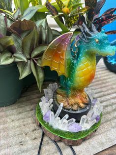 a colorful dragon figurine sitting on top of a table next to potted plants