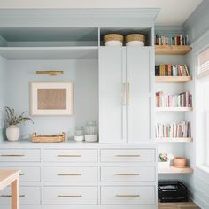 a kitchen with white cabinets and shelves filled with books