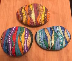 three painted rocks sitting on top of a wooden table