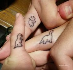 two people holding hands with tattoos on their fingers and one has a small dog in the middle