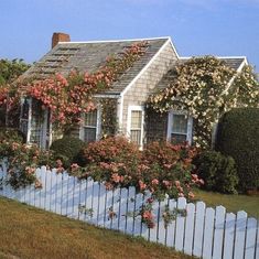 a white picket fence surrounds a house with pink flowers on it