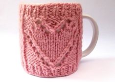 a pink knitted mug cozys up in the shape of a heart on a white background