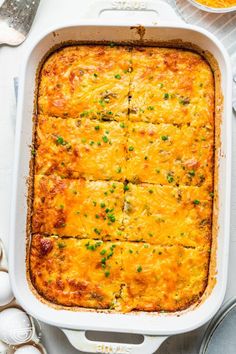 a casserole dish with cheese and green onions in it on a white table