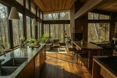 a kitchen and dining area with large windows overlooking the woods in the background, along with wooden flooring