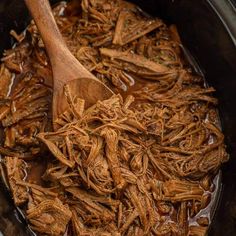 shredded meat in a slow cooker with a wooden spoon