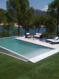 an empty swimming pool in the middle of some grass with lounge chairs and trees around it