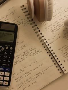 a calculator, pen and headphones on top of an open notebook with handwritten notes