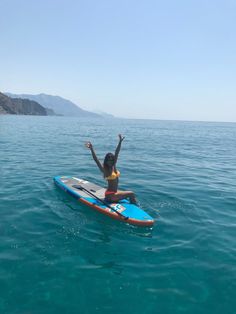 a woman sitting on a surfboard in the ocean with her arms raised above her head