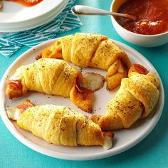 pigs in a blanket on a plate next to a bowl of tomato sauce and a spoon