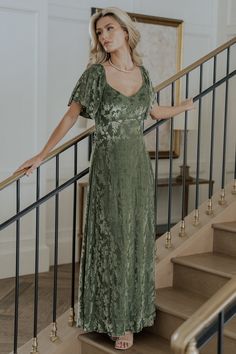 a woman in a green dress standing on the stairs with her arms out and looking at the camera