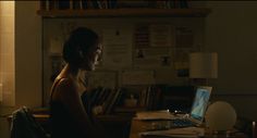 a woman sitting at a desk with a laptop computer in front of her and bookshelves behind her