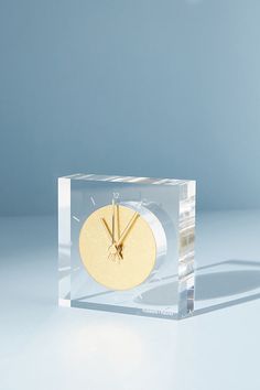 a clear clock with gold hands on a white table top, in front of a blue background