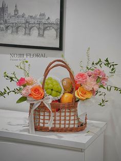 a basket filled with fruit and flowers sitting on top of a table next to a painting