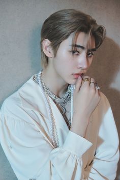 a young man in a white shirt is posing with his hands on his chin and wearing pearls