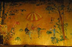 a painting on the wall of a restaurant with people sitting at a table under an umbrella