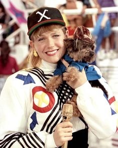 a woman holding a small dog wearing a hat and sweater while standing in front of a crowd