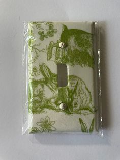 a single light switch cover with an image of animals on green and white fabric in the background