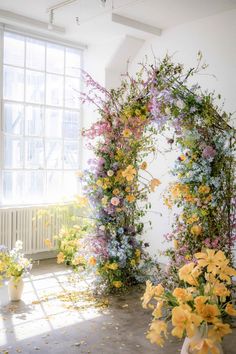 an arch made out of flowers is shown in front of a window with sunlight streaming through it