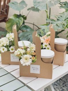 three brown paper bags with flowers in them sitting on a table next to some plants