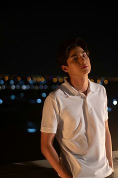 a young man wearing a white shirt and tie standing in front of a city at night