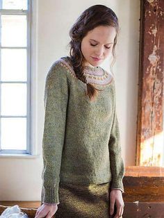 a woman standing in front of a window wearing a green sweater and skirt with an embroidered collar