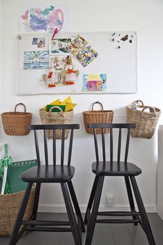 two wooden chairs sitting next to each other in front of a wall with pictures on it