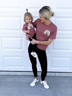 a woman holding a baby in her arms and wearing a maroon t - shirt with the letter m on it