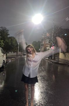 a woman is walking in the rain with her arms spread out and she is holding an umbrella over her head