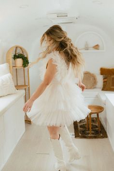 a woman standing in a room wearing white boots and a tulle dress with long sleeves