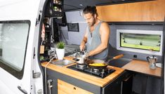 a man preparing food in the back of a camper van with its door open