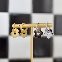 three pairs of earrings are hanging on a gold stand in front of a checkered wall