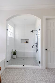 a white bathroom with an arched shower door and tiled floor, along with a potted plant in the corner