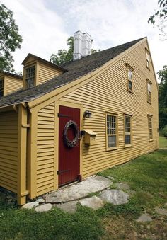 a yellow house with a red door and wreath on it's front porch in the country