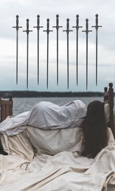 a woman laying on top of a bed covered in white sheets next to tall poles