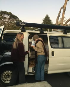 two people standing in the back of a white van with open doors and food inside