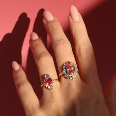 This bespoke ring features so many unique gemstones. Bezel set in the center is a 3.54ct oval pink sapphire, surrounded by white diamond epaulettes, white diamond baguettes, round padparadascha sapphires, and round pink sapphires. A true statement piece. Please note resizing this ring adds an extra 7-10 days for delivery. Heirloom Pink Sapphire Round Ring, Fine Jewelry Yellow Gold Pink Sapphire Diamond Ring, Pink Sapphire Fine Jewelry Ring, Heirloom Yellow Gold Pink Sapphire Ring, Fine Jewelry Pink Sapphire Red Ring, Ballerina Ring, Padparadscha Sapphire, Bespoke Rings, Peachy Pink