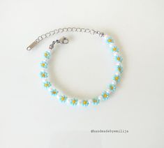 a blue bracelet with yellow and white flowers is shown on a white surface, next to a key chain