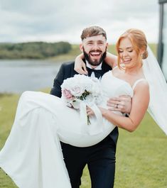 a bride carrying her groom on his back in front of the water at their wedding