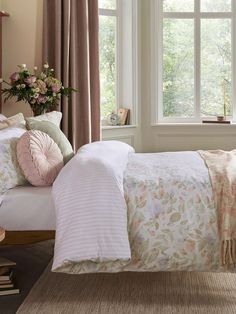 there is a bed with pink and white comforter in the room next to two windows