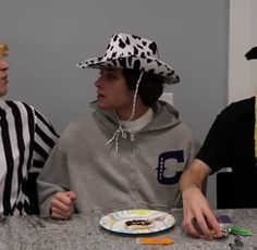 three people sitting at a table with plates and hats on their heads, one wearing a zebra print hat