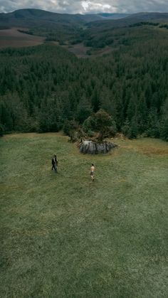 two people are walking in the grass near some trees