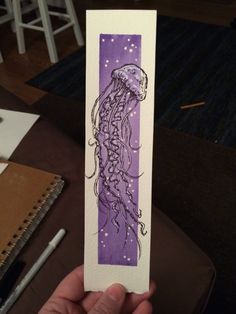 a drawing of a jellyfish in purple watercolor on white paper, held up by a person's hand