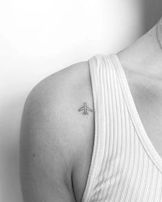 a black and white photo of a woman's shoulder with a small airplane tattoo on it