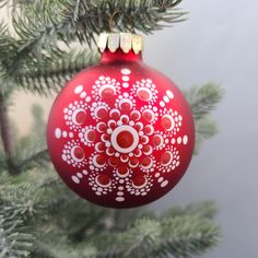 a red christmas ornament hanging from a pine tree's branch with snowflakes on it